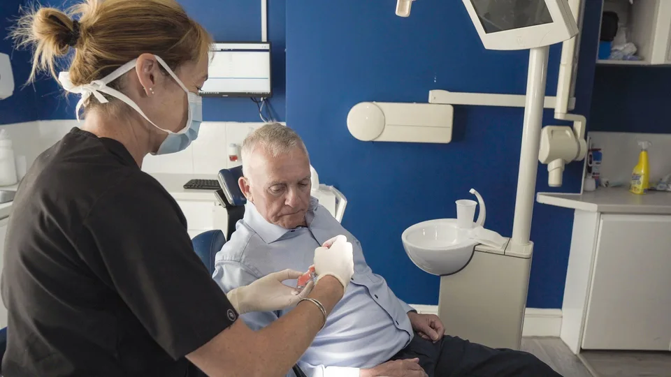 Dental professional explaining tooth implant model to elderly patient in Dublin clinic